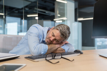 Fototapeta premium Tired senior boss businessman sleeping on desktop in office