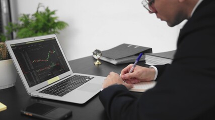 A close-up of the laptop screen, where a graph of bitcoin transaction statistics is visible. A business man