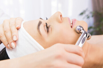Obraz na płótnie Canvas Hands of professional cosmetologist using facial roller massage instrument applying to the woman face in a beauty clinic salon.