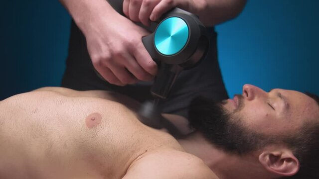 Close-up of a Caucasian male pectoral muscle percussion massager working out in a professional massage parlor