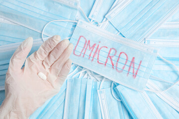 Photo of a hand in glove holds one tablet and many medical protective masks lying on the table with...
