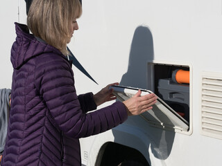 Obraz premium A lady motor homer closes the external locker door of her motorhome recreational vehicle.Cassette toilet visible insideRV.