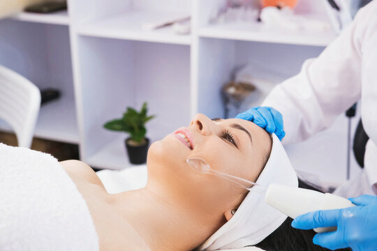 Closeup photo of professional female cosmetologist doing darsonval electric facial vacuum procedure in cosmetology clinic wearing blue gloves.