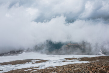 Dramatic landscape with people inside cloud above motley mountain valley. Tourists in cloud above multicolor valley. Low cloud on stone hill with snow. Awesome high mountain scenery in low clouds.