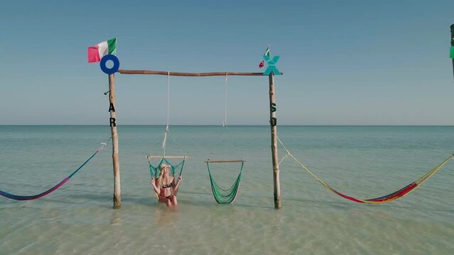 Female tourist with straw hat in bikini swinging in chair, Holbox Hammocks