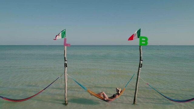 Female tourist with straw hat laying in Holbox hammocks, sunny day