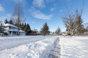 Fototapeta na wymiar Residential Neighborhood in the Suburbs with White Snow covered road. Sunny Sunrise. Taken in Fraser Heights, Surrey, Vancouver, BC, Canada.