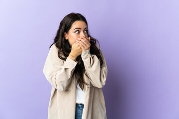 Young caucasian woman isolated on purple background covering mouth and looking to the side