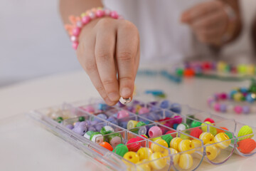 Little girl making beaded jewelry at table, closeup