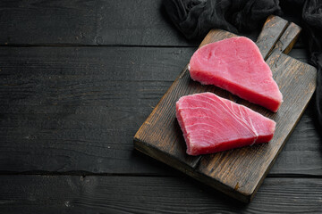Pieces of raw tuna fish, on wooden cutting board, on black wooden background , with copyspace  and...