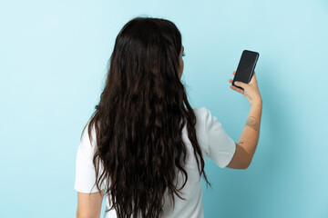 Young woman using mobile phone isolated on blue background in back position