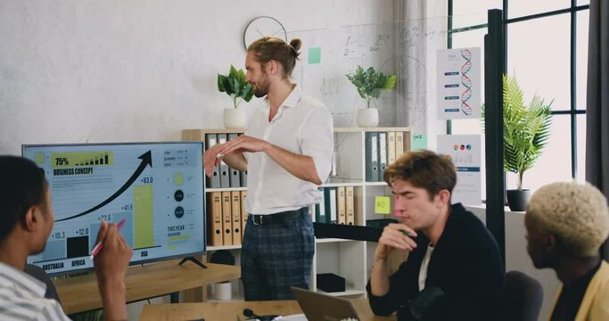 Handsome young male manager leading making a presentation to his colleagues using glassboard and digital whiteboard during creative brainstorming modern office meeting