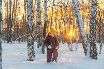 a girl in a warm jumpsuit walks through a winter snow-covered forest