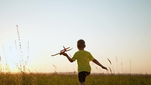 child runs with silhouette toy airplane in park field. childhood kid dream happy family concept. boy running with toy airplane in park at sunset. boy kid play dream of sunlight becoming a pilot