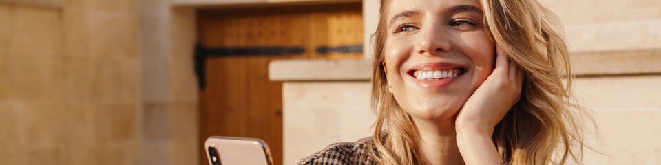 Smiling blonde young woman holding mobile phone