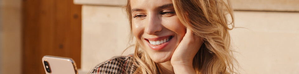 Smiling blonde young woman holding mobile phone
