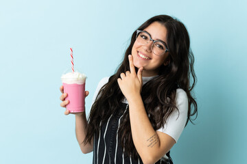 Young woman with strawberry milkshake isolated on blue background happy and smiling