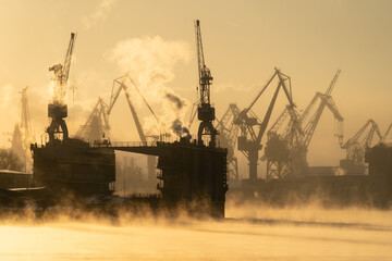 Cranes of Baltic shipyard in St. Petersburg in frosty winter day, steam over the Neva river, smooth...