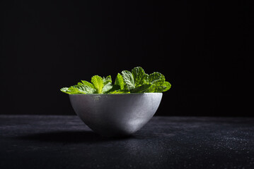 Tazón de plata lleno de hojas de menta verde fresca sobre fondo negro. Aislado © R. Guas