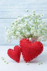 Happy Valentine`s Day holiday card. Two red felt hearts and a bouquet of gypsophila flowers on a light background.