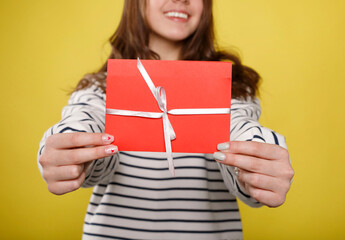 Happy young teenager girl holds red gift certificate on yellow background. People lifestyle...