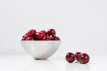 Cerezas dulces rojas en un recipiente de plata y fondo blanco