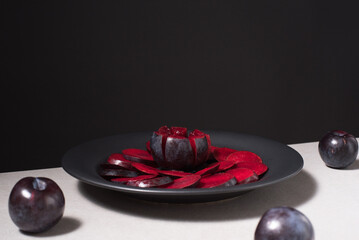 Rodajas de ciruelas negras y ciruelas enteras en un plato negro sobre una mesa gris