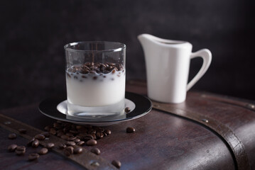 Vaso de leche con granos de café y una lechera sobre una maleta marrón