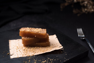 Dulce pasta de gelatina de membrillo dorado con sésamo molido y un tenedor sobre una placa de madera negra