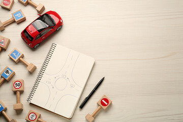 Many different miniature road signs, notebook and toy car on white wooden background, flat lay with...