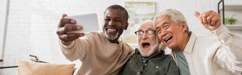 Positive multicultural men using mobile phone at home, banner.