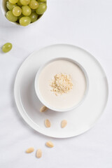 Crema de almendras, sopa fría española. Ajo blanco de Málaga con almendras y uvas en un recipiente blanco sobre una mesa blanca	