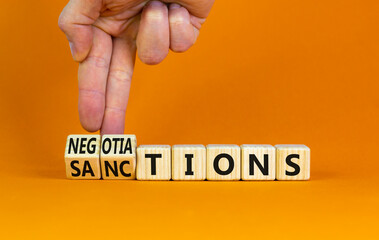 Sanctions or negotiations symbol. Businessman turns cubes, changes the word sanctions to negotiations. Beautiful orange table, orange background, copy space. Business, sanction or negotiation concept.
