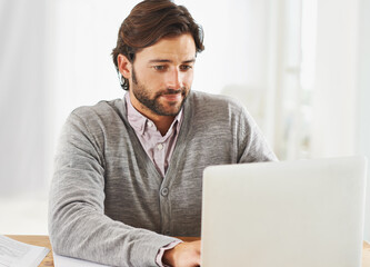 Connected to the world. A handsome businessman sitting at his desk and working on his laptop.