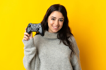Woman playing with a video game controllerisolrted on yellow background smiling a lot © luismolinero