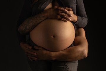 Man embraces the belly of a pregnant woman in a dark background with a warm light