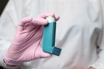 A woman's hand in a glove, the doctor's hand holds an asthma inhaler. Using a blue asthma inhaler to relieve an asthma attack