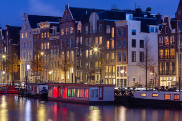 Obraz premium Beautiful old houses on the city waterfront of Amsterdam at sunset.