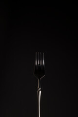 Stylish steel black fork on a dark background. Close-up. Monochrome. Vertical position. Copy space.
