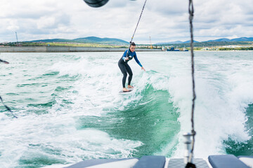 Watersport concept. Young athletic woman learning wakesurfing and perfecting tricks. Female in...