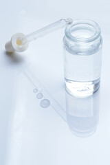 glass transparent jar and a cosmetic pipette with liquid droplets on a white background.