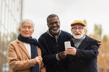 Multiethnic pensioners with smartphone looking at camera on urban street.