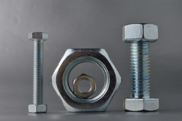 composition of new bolts and nuts of different sizes on a gray background.