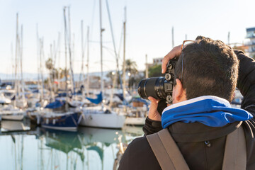 Rear view of a middle-aged man taking photos with a professional reflex camera in a port at sunset