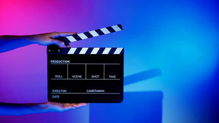 Blurry images of movie slate or clapper board. Hand holds empty film making clapperboard on color...