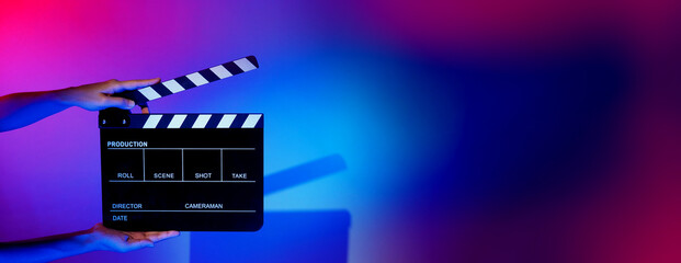 Blurry images of movie slate or clapper board. Hand holds empty film making clapperboard on color background in studio for film movie shooting or recording. Film slate for Youtuber video production. - obrazy, fototapety, plakaty