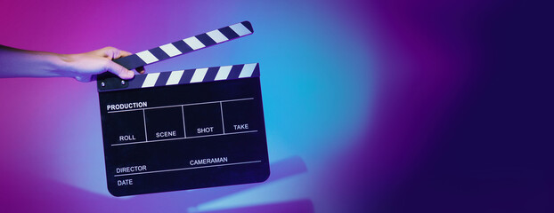 Blurry images of movie slate or clapper board. Hand holds empty film making clapperboard on color...