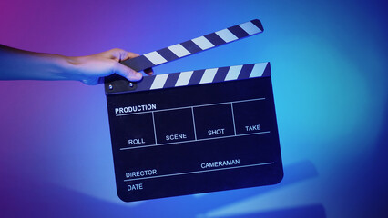Obraz premium Blurry images of movie slate or clapper board. Hand holds empty film making clapperboard on color background in studio for film movie shooting or recording. Film slate for Youtuber video production.