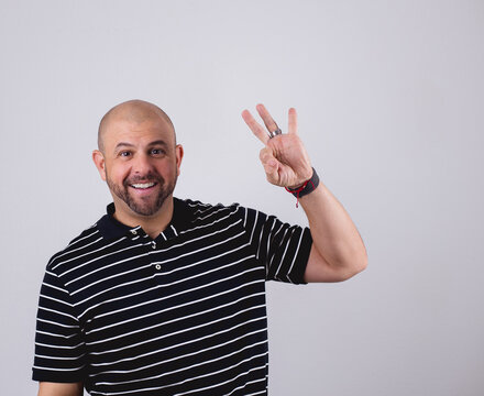 Hispanic bald  man standing in front of a white background and making emotional gestures holding three fingers stock photo royalty free 