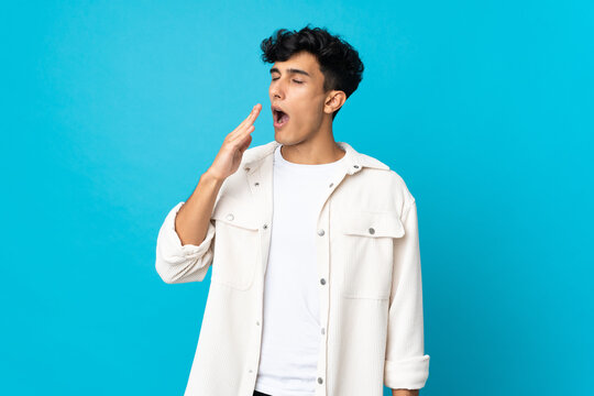 Young Argentinian man isolated on background yawning and covering wide open mouth with hand